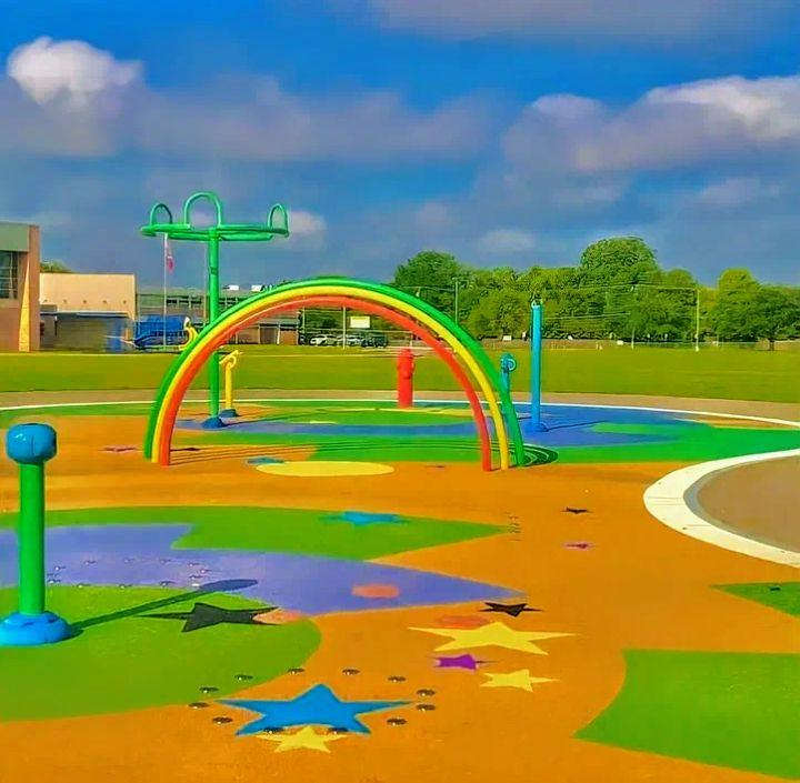 A bright outdoor theme park splash area with rainbow arches.