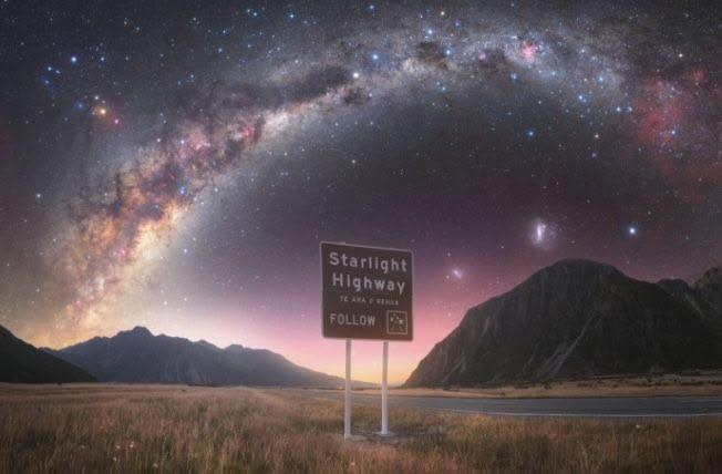 A starlight highway sign below a bright galaxy in the night sky.